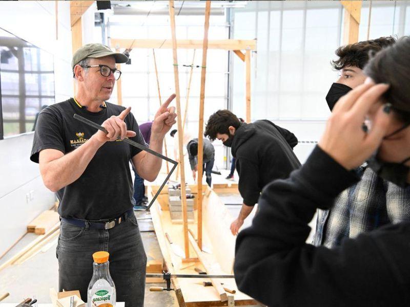 Students listening to man teach about building wooden boats